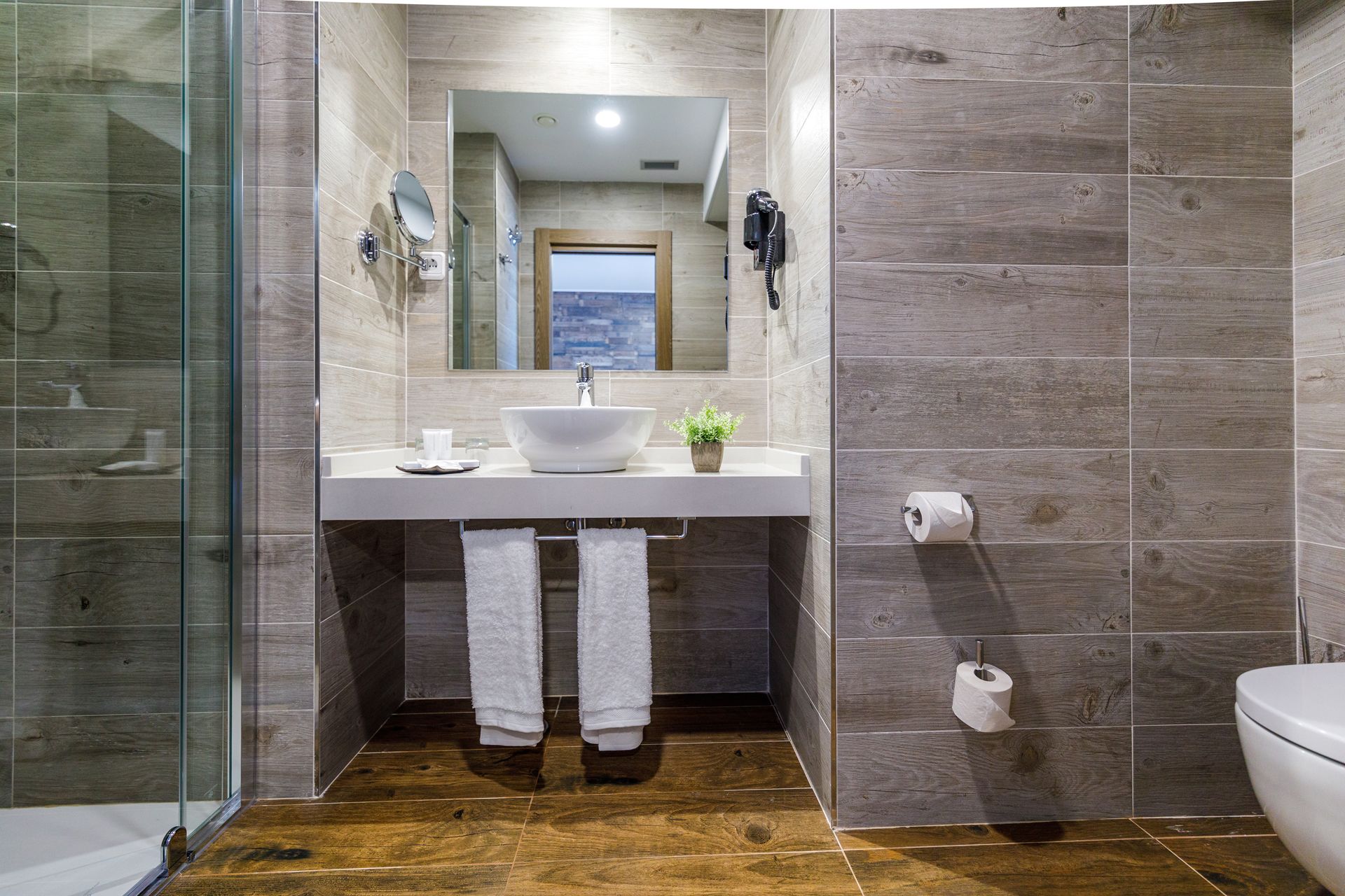 Un baño moderno con un espejo grande, un lavabo blanco y una cabina de ducha de vidrio.