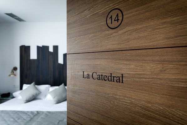 Habitación de hotel con cama, almohadas y un panel de madera con el número 14 y el nombre 'La Catedral'.