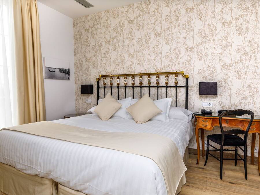 Una cama bien hecha con cabecera, una mesita de noche con lámpara y una silla.