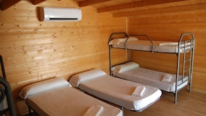 A wooden cabin room with bunk beds and a single bed, an air conditioning unit on the wall, and a wooden floor. - Camping ValdeArenas (Iznajar)