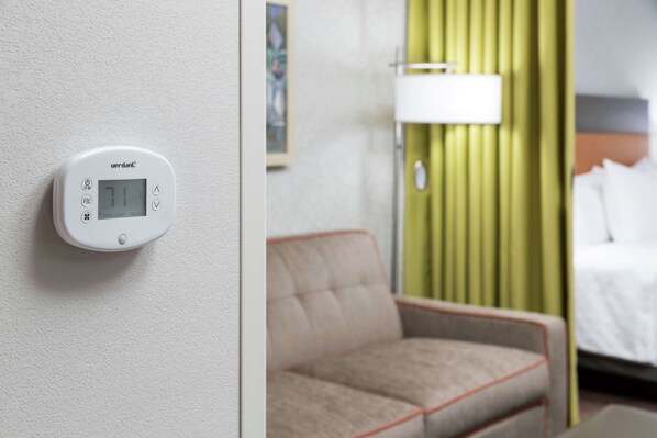 A thermostat on a wall, a beige armchair, and a bed with white bedding.