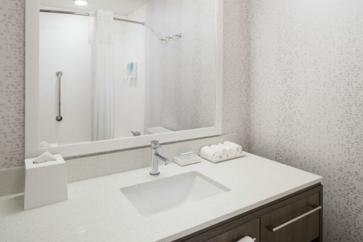 Un baño moderno con un espejo grande, un lavamanos y una zona de ducha.