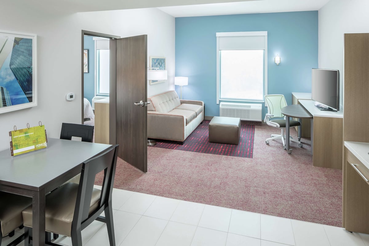 A hotel room with a dining table, a sofa, a desk, and a TV.