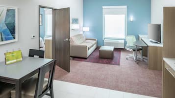 A hotel room with a dining table, a sofa, a desk, and a TV.