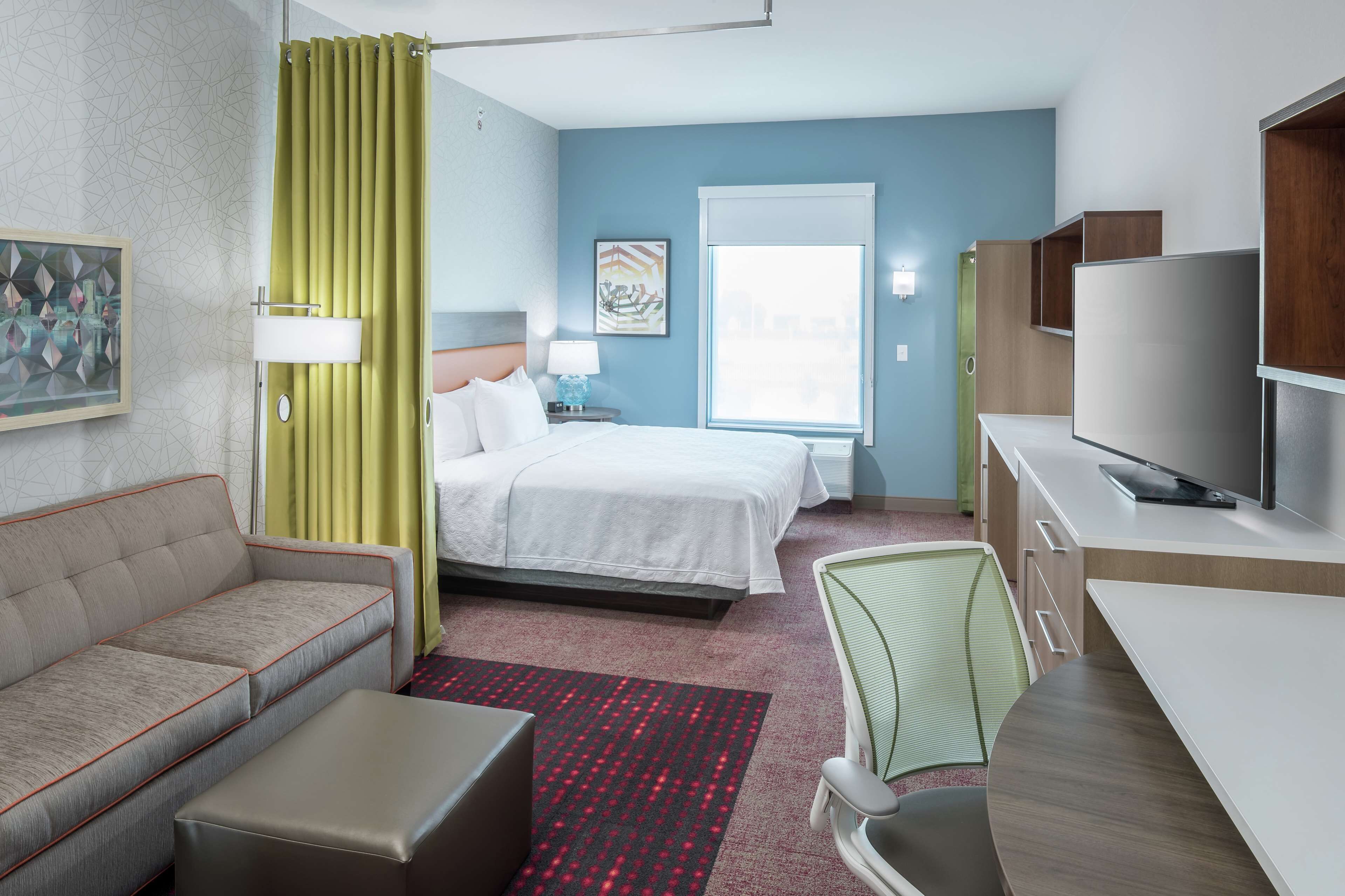 A hotel room with a bed, a sofa, a desk, a TV, and a window.
