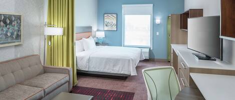 A hotel room with a bed, a sofa, a desk, a TV, and a window.