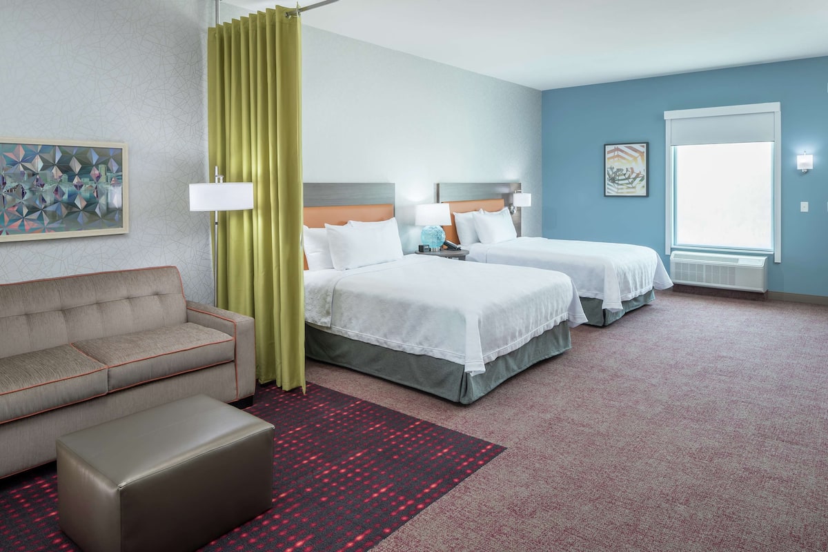 A hotel room with two beds, a sofa, a red patterned rug, and artwork on the walls.