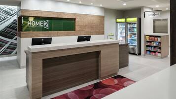 Bancada de recepção de hotel com visor digital, geladeira e bar de lanches.