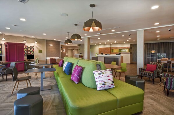 A modern hotel lobby with a green sofa, dining area, and reception desk.