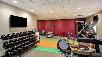 A gym with weightlifting equipment, treadmills, and a television on the wall.