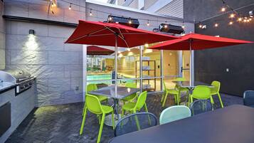 An outdoor patio with a grill, bright green chairs, and red umbrellas.
