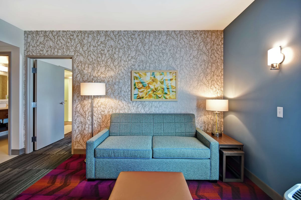 Een kamer met een turquoise bank, twee wandlampen, een lijst met abstract schilderij en een kamerbreed tapijt met dessin.
