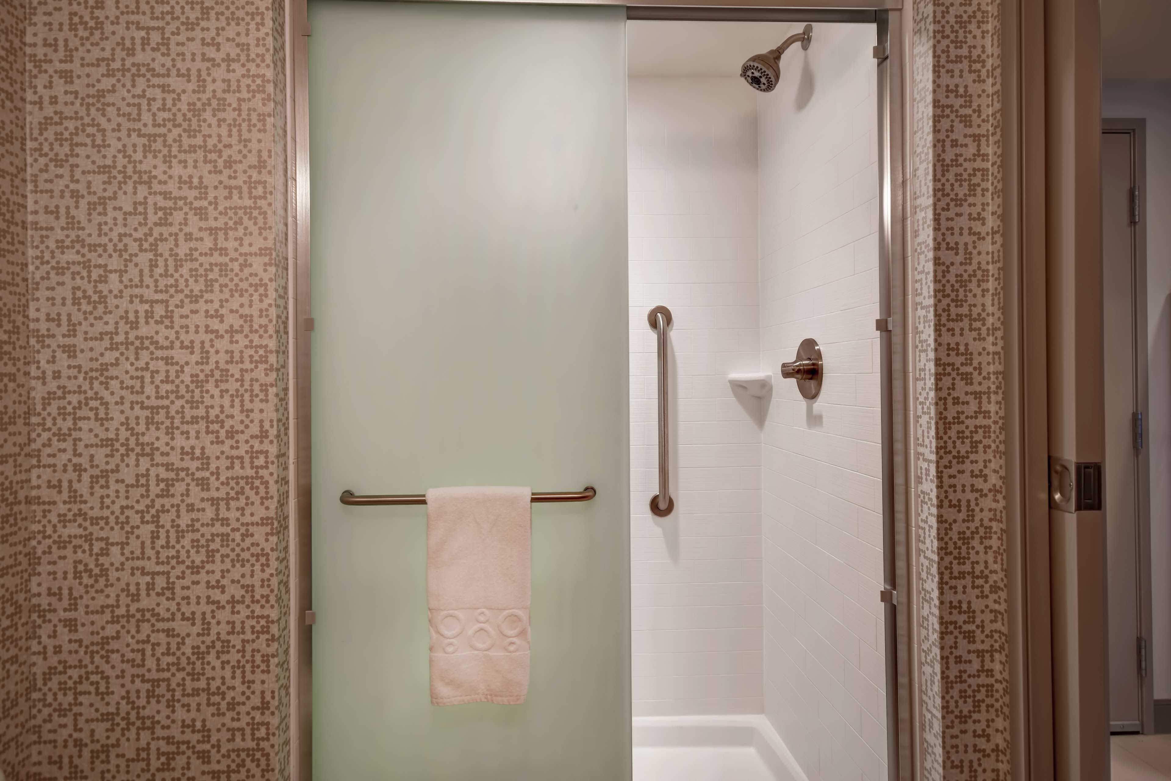 Une salle de bain avec une porte en verre, un porte-serviettes avec une serviette, un espace douche et des toilettes.