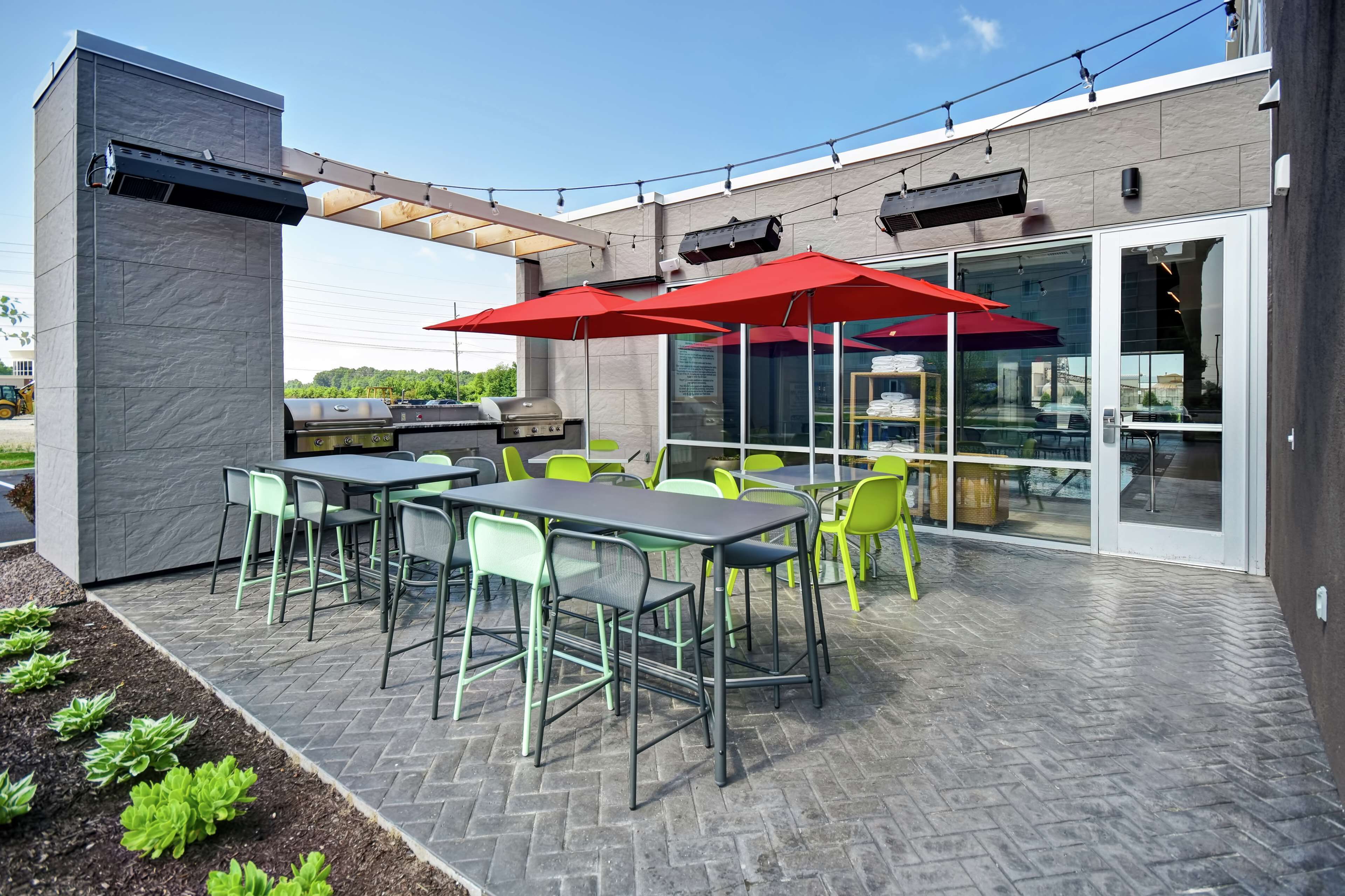 Un patio al aire libre con mesas y sillas, una parrilla y luces colgantes.