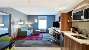 Una habitación de hotel moderna con kitchenette, una cama, un sofá, un escritorio y un ventanal grande.