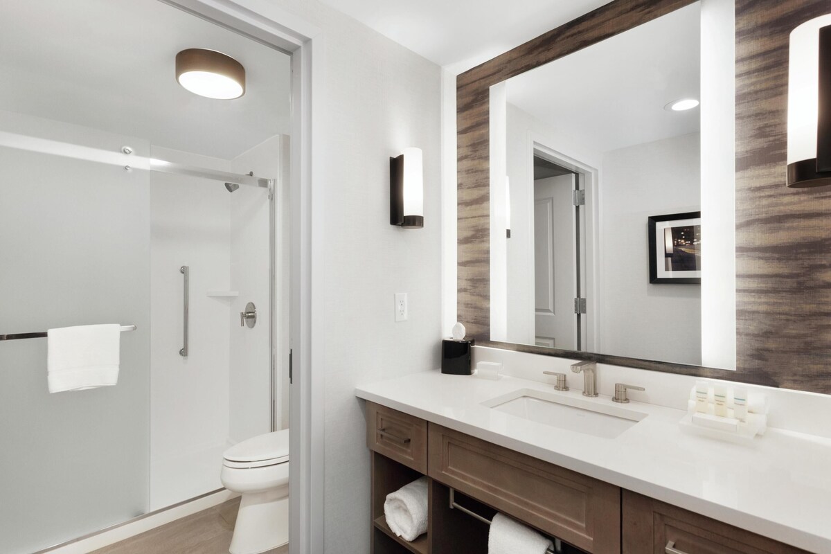 Une salle de bain moderne avec une douche à parois de verre, des toilettes blanches, un grand miroir avec un cadre en bois et un lavabo blanc avec un meuble-vasque.