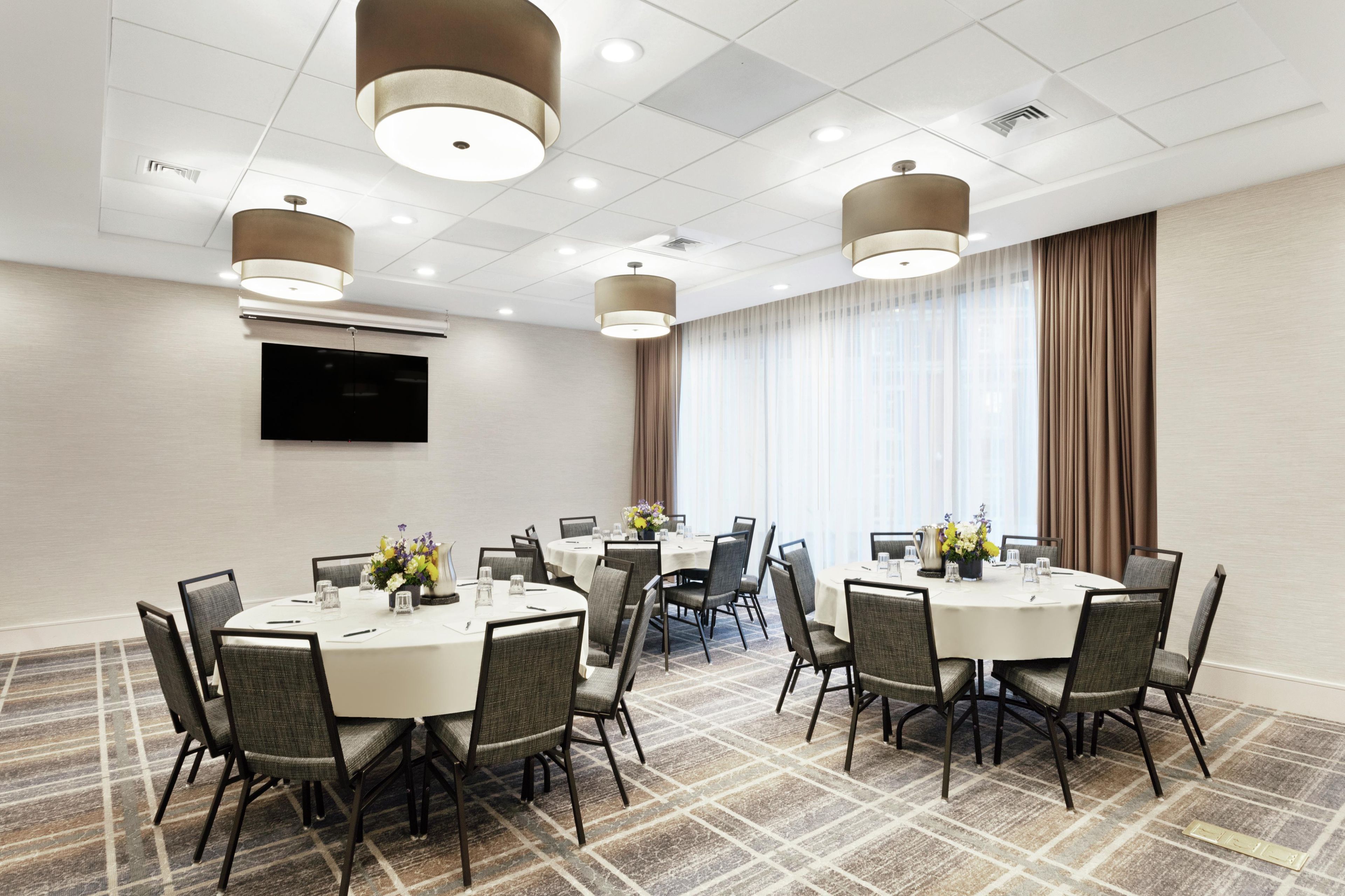A conference room with round tables, chairs, and a flat-screen TV on the wall.