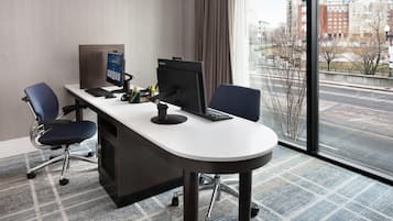 Habitación de hotel moderna con escritorio, dos sillas, una computadora y un ventanal con vistas a la ciudad.