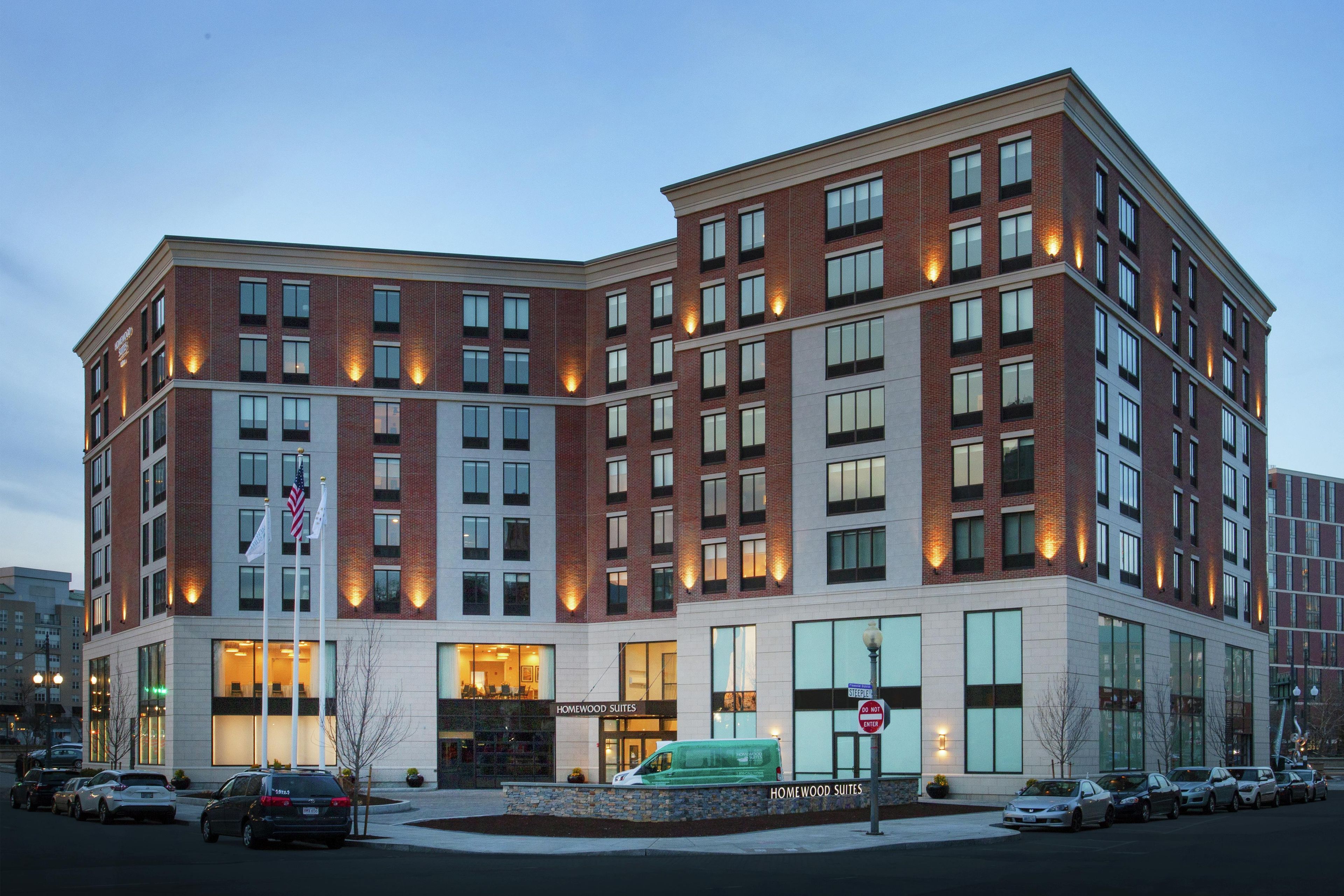 Een meerhoog hotel met een bakstenen gevel, grote ramen en een bord met de tekst 'Homewood Suites'.