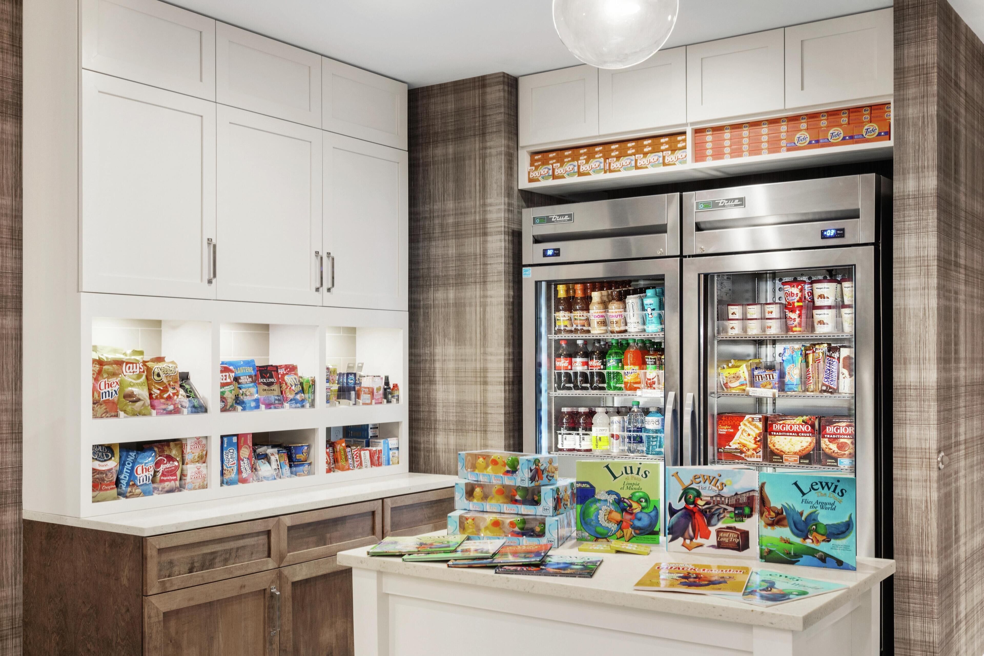 A kitchen with white cabinets, a refrigerator stocked with food, and a counter with children's books and snacks.