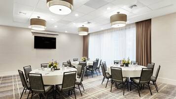 A conference room with round tables, chairs, and a flat-screen TV on the wall.