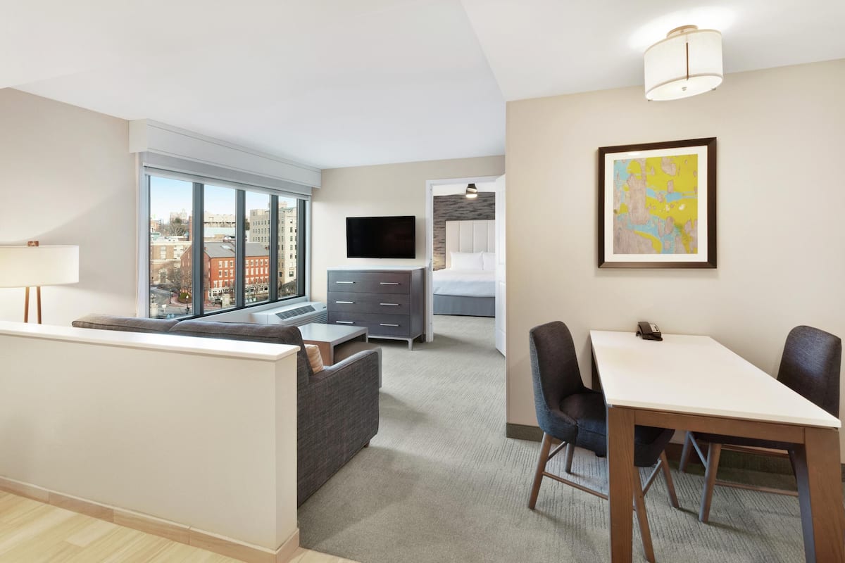 Une chambre d’hôtel moderne dotée d’une grande fenêtre, d’un lit, d’un bureau et d’un coin repas.