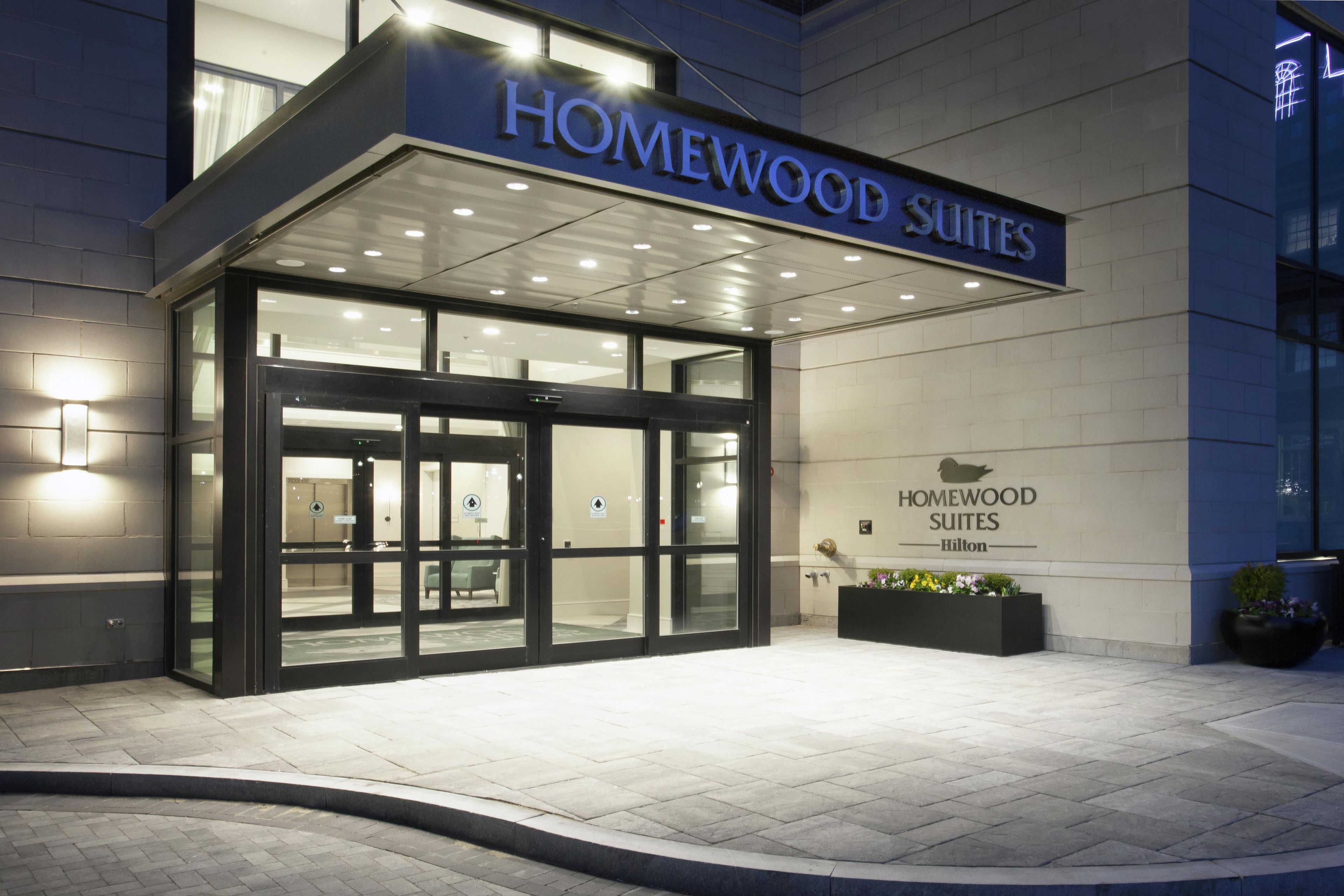 Een hotelentree met een glazen deur en een bord waarop 'Homewood Suites' staat.