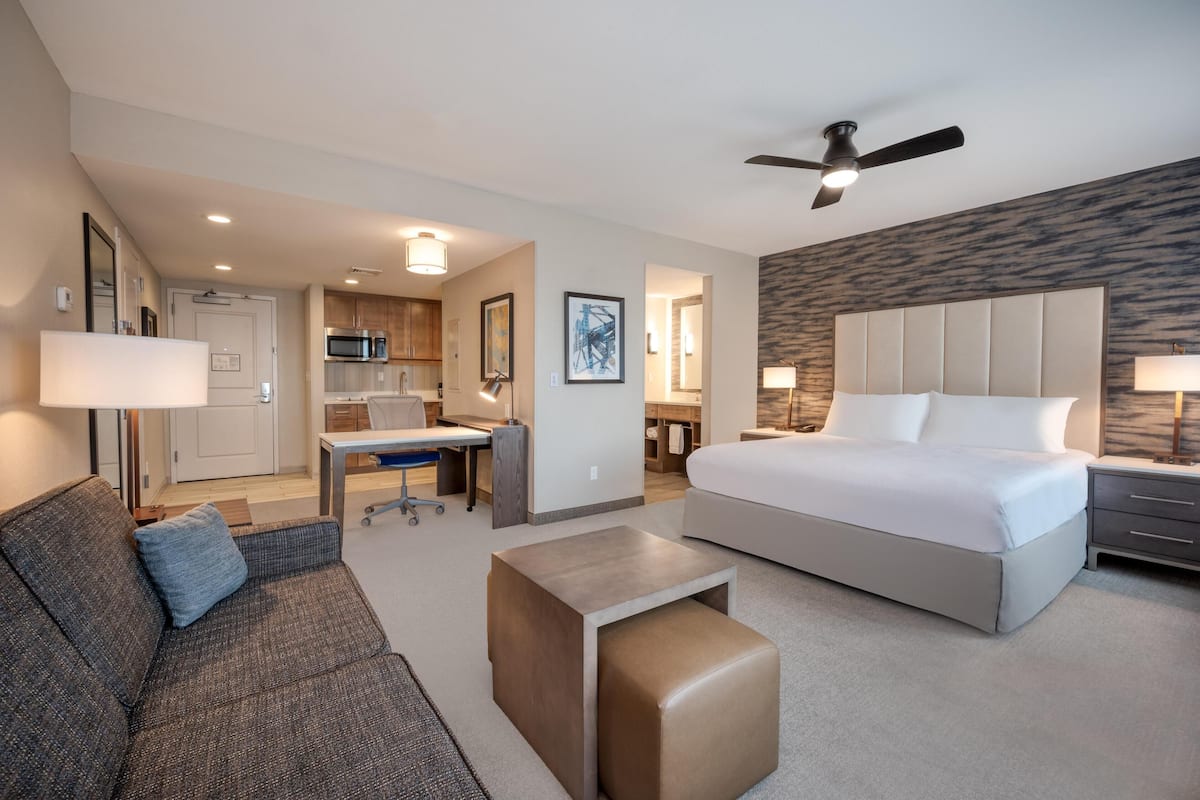 Une chambre d’hôtel comprenant un lit, un bureau, une kitchenette et un coin salon avec un canapé et une table basse.