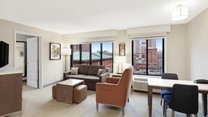 A modern hotel room with a living area, a dining table, and large windows offering city views. - Homewood Suites by Hilton Providence Downtown (Providence)
