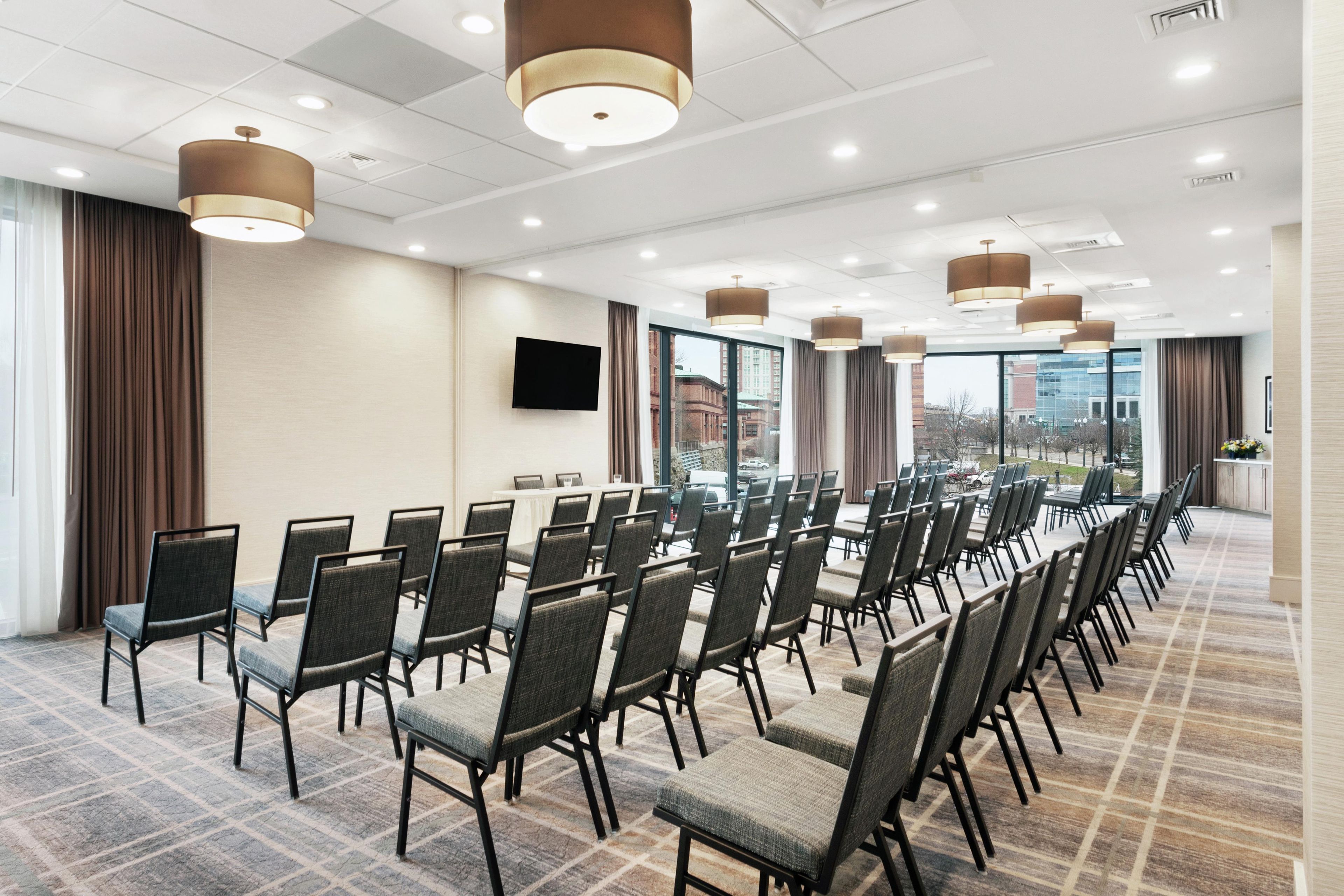 Un salón de conferencias con filas de sillas, una mesa larga y ventanas amplias que ofrecen vistas de la ciudad.
