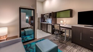 Habitación de hotel compacta con cama, escritorio, televisión, microondas y kitchenette pequeña.