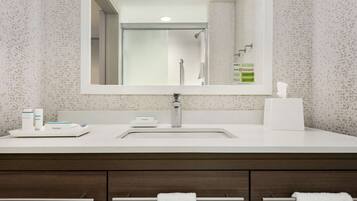 Un baño con un espejo grande, un lavabo y un mueble de tocador con cajones. Hay un perchero con dos toallas.