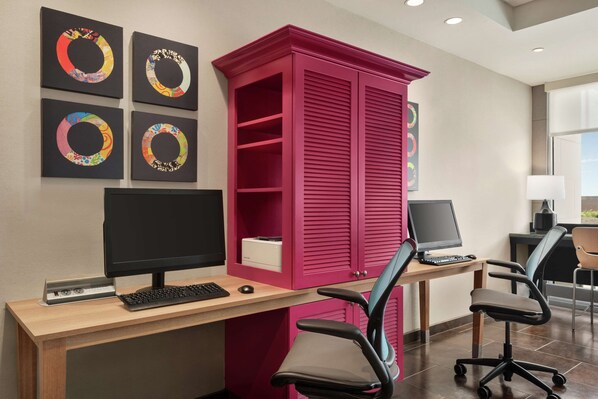 Ein Arbeitsplatz mit zwei Schreibtischen, Computern und Bürostühlen. Vier gerahmte, runde Kunstwerke sind an der Wand angebracht.