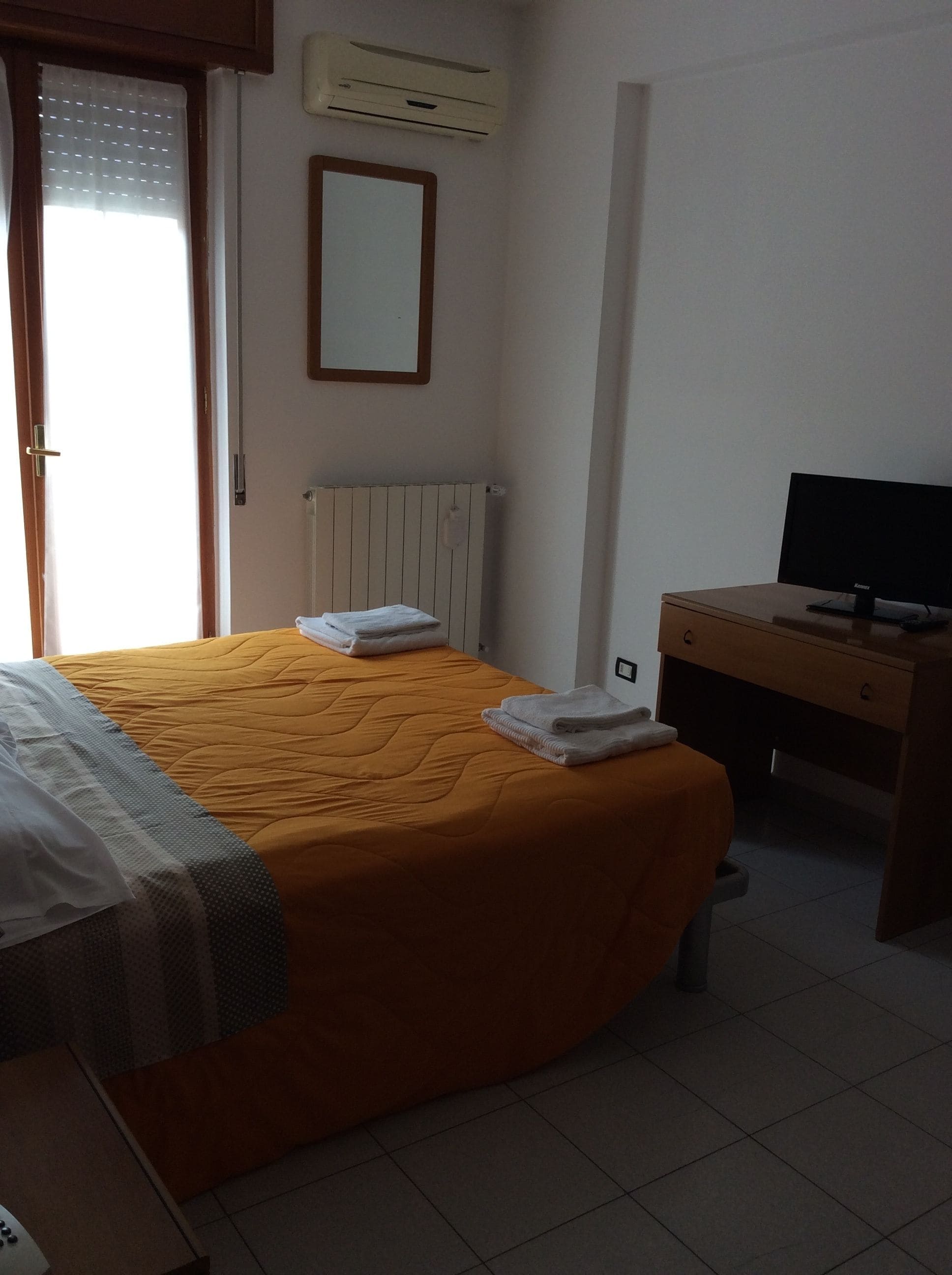 Une chambre d’hôtel équipée d’un lit, d’un bureau avec un ordinateur, d’un radiateur et d’un appareil de climatisation.