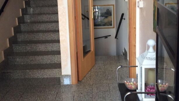 Un escalier menant à une pièce dotée d’une porte en bois, d’une petite table sur laquelle se trouve une lampe blanche, et d’un tableau accroché au mur.
