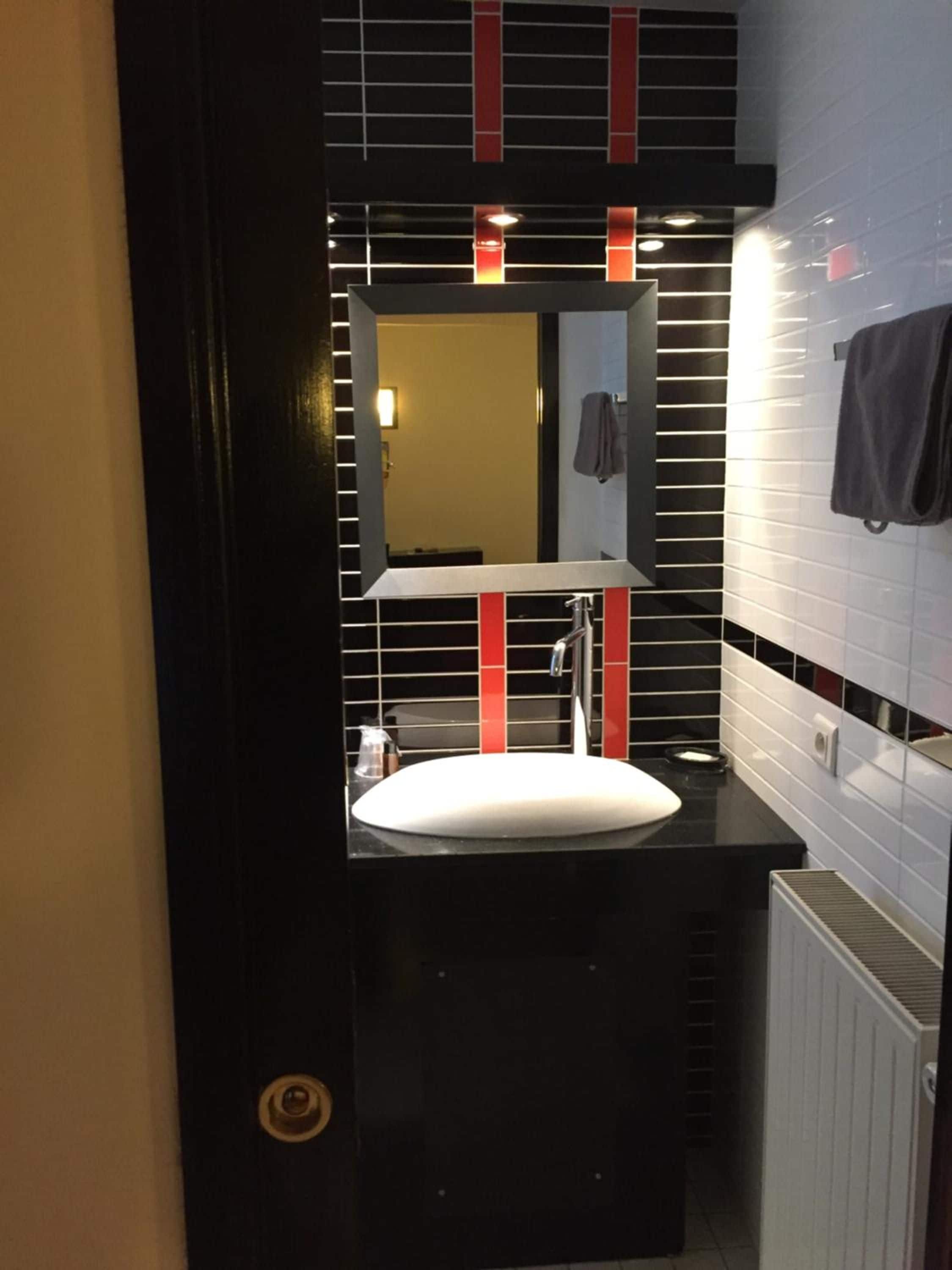 Un baño con un lavamanos blanco, un espejo y detalles rojos en la pared.