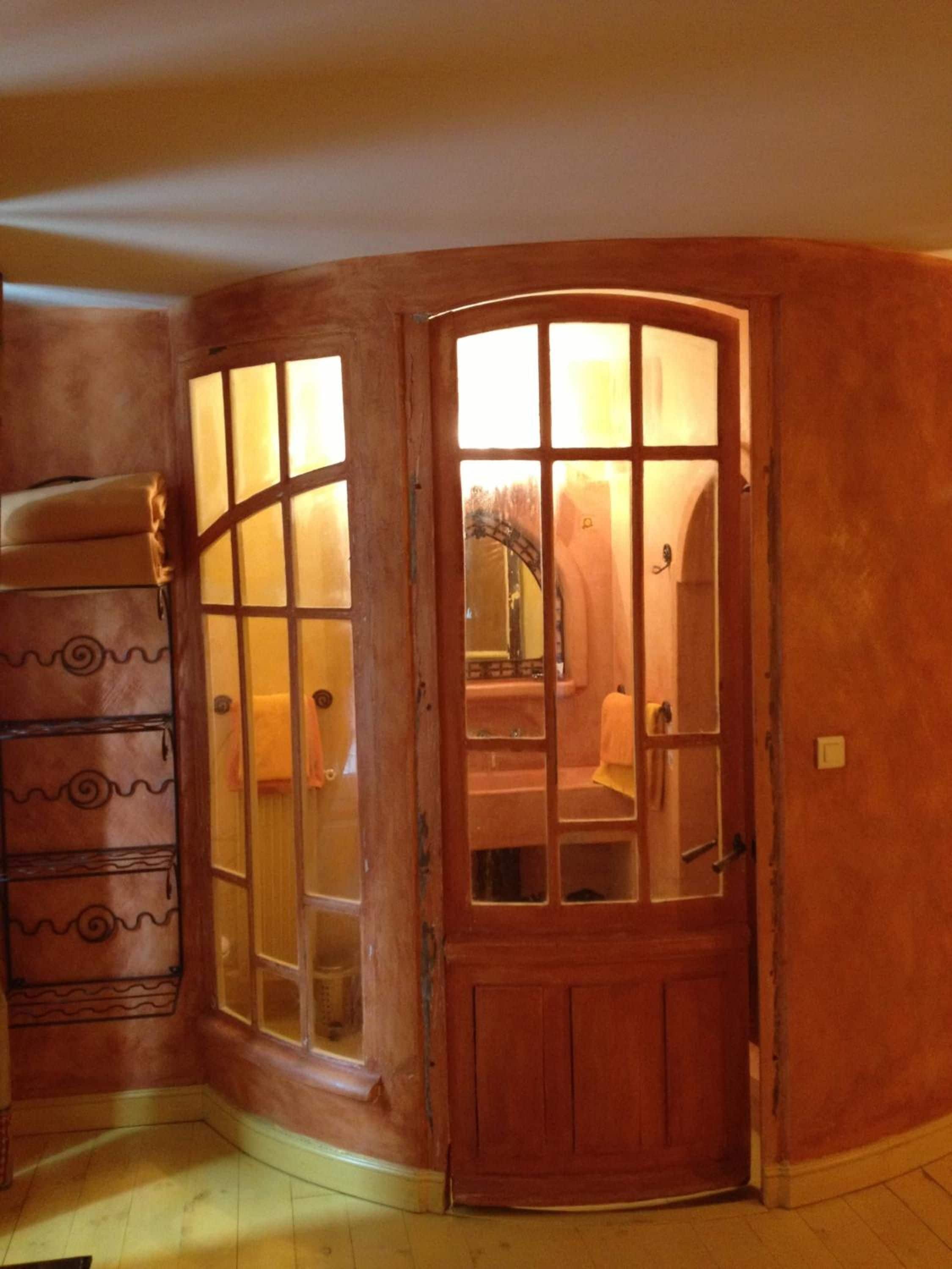 Una habitación de esquina con una puerta de madera que da a un baño, un pequeño sofá y un papel tapiz decorado.