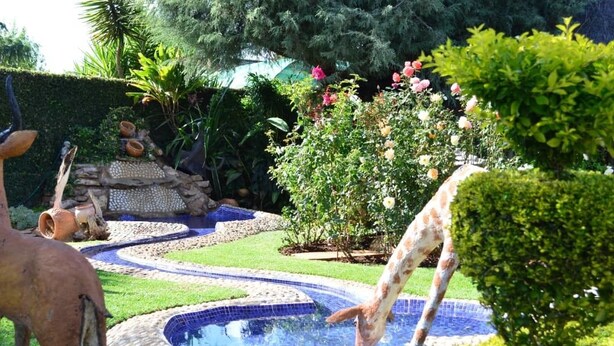 A garden with a swimming pool, decorative statues, and lush greenery. - Padandaro Guest House (Bulawayo)