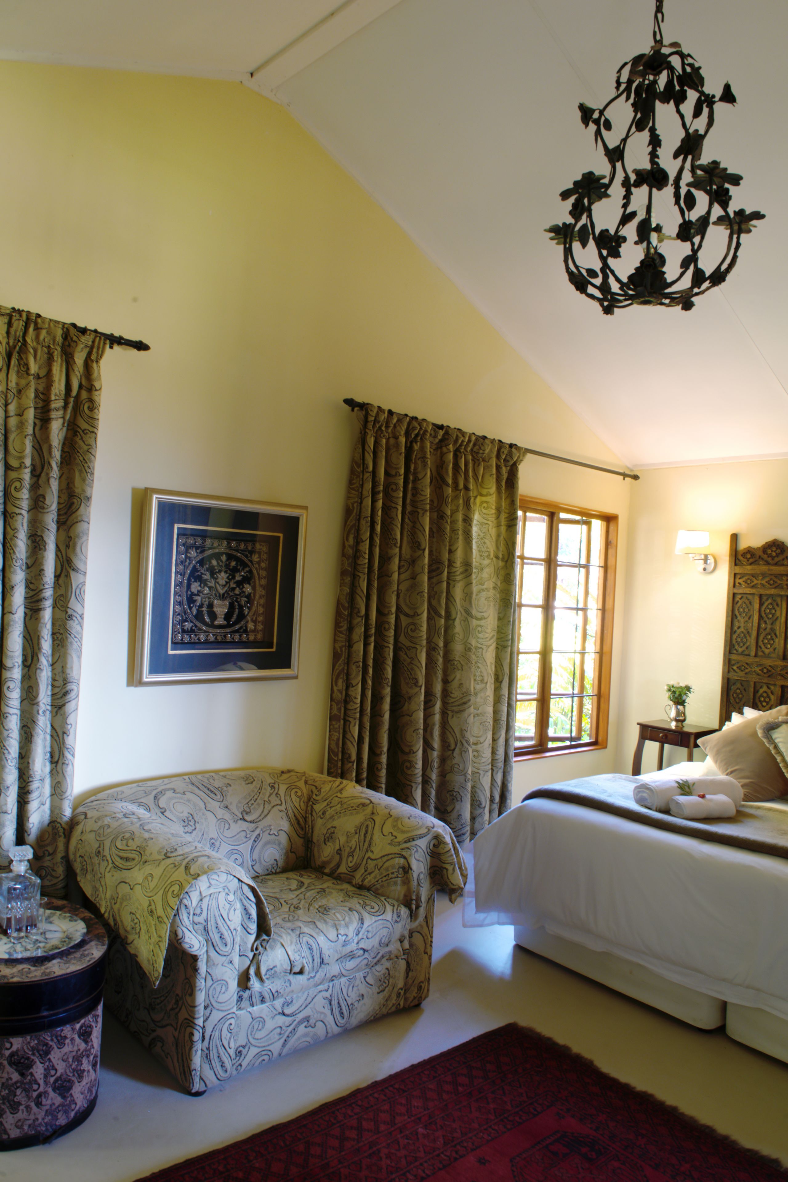 A bedroom with a bed, a chair, a window, and a chandelier.