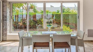 A dining area with a glass table and wicker chairs, large windows with a view of a garden. - Cozy home in St Florent (St Florent)