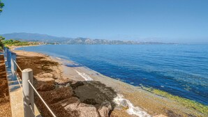 A coastal beach with clear blue waters, rocky shoreline, and distant mountains. - Cozy home in St Florent (St Florent)