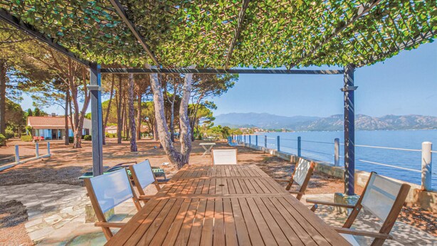 An outdoor wooden deck with benches, a pergola, and a view of the sea. - Cozy home in St Florent (St Florent)