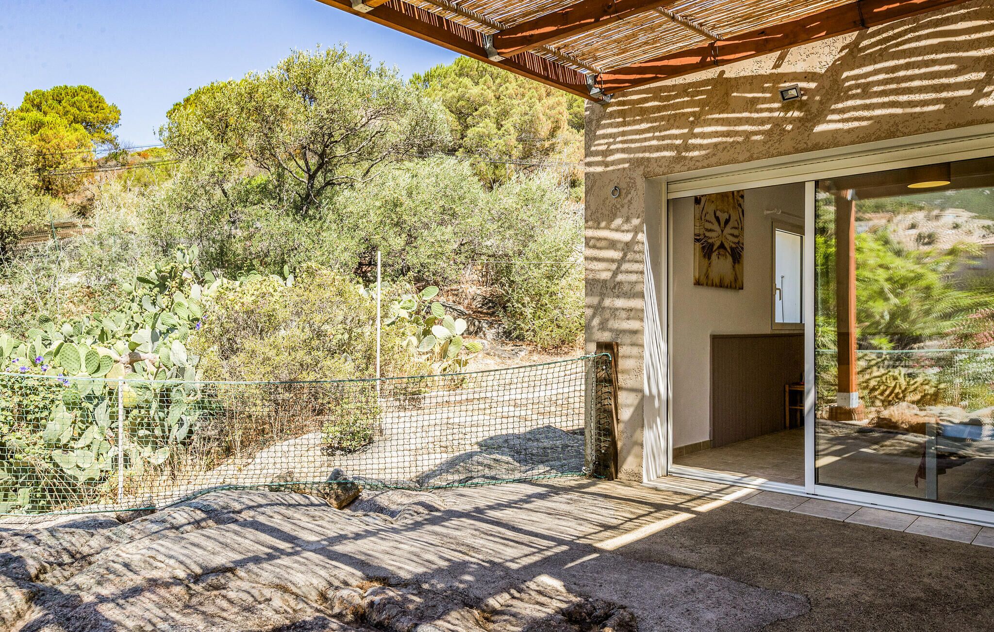 Un edificio con patio, entrada por puerta de vidrio y vista a un paisaje natural con árboles y cactus.