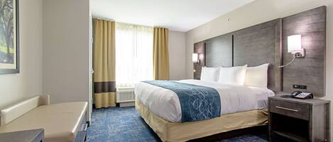 A hotel room with a bed, bedside table, lamp, and a desk.