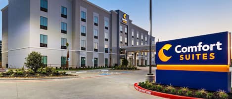 A Comfort Suites hotel with a modern facade, a clear sky, and a sign indicating a tow-away zone.
