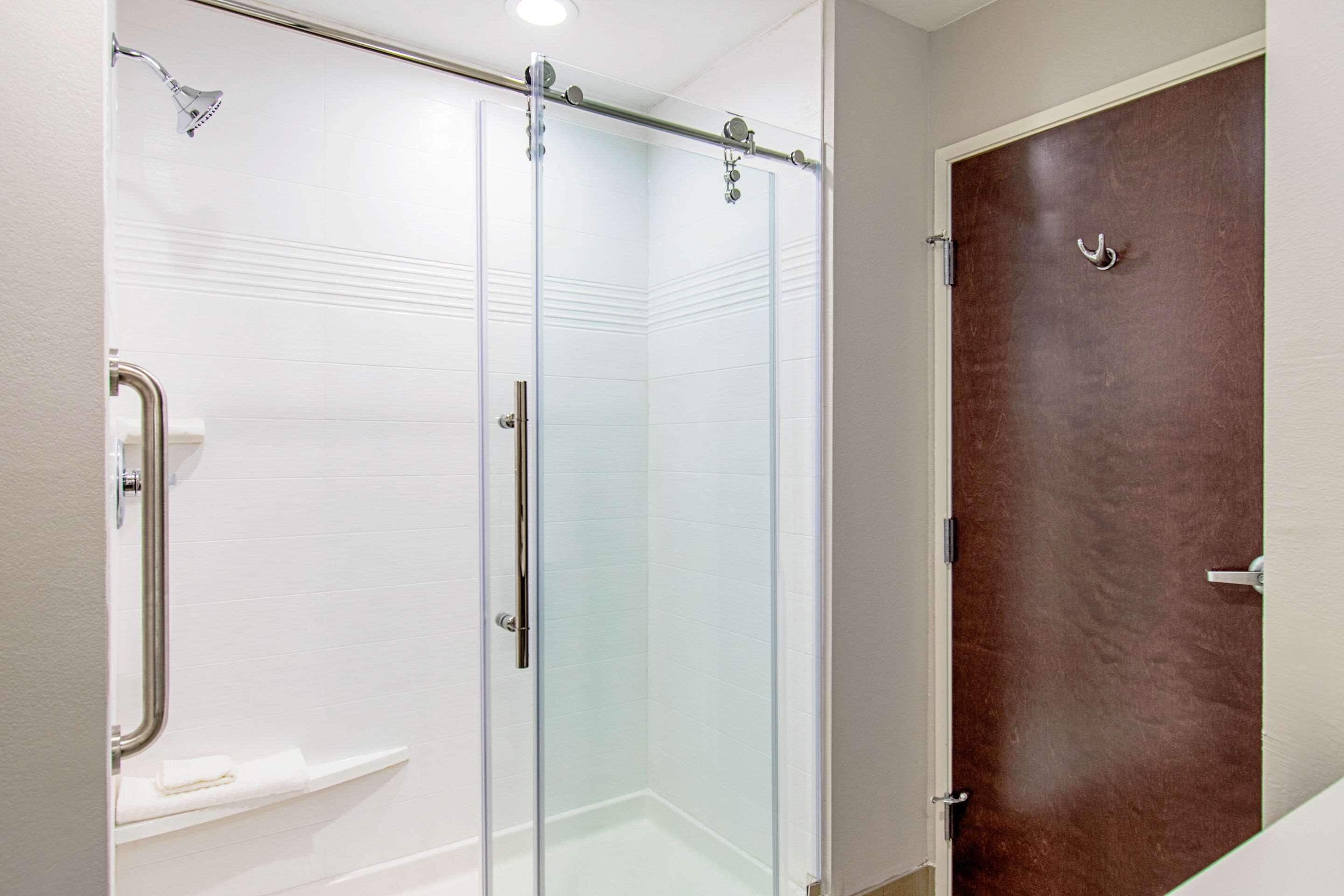 A glass-enclosed shower with a handheld showerhead, a white towel rack, and a brown door.
