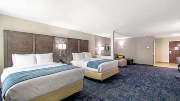 A hotel room with two beds, a desk, a chair, and a small seating area.