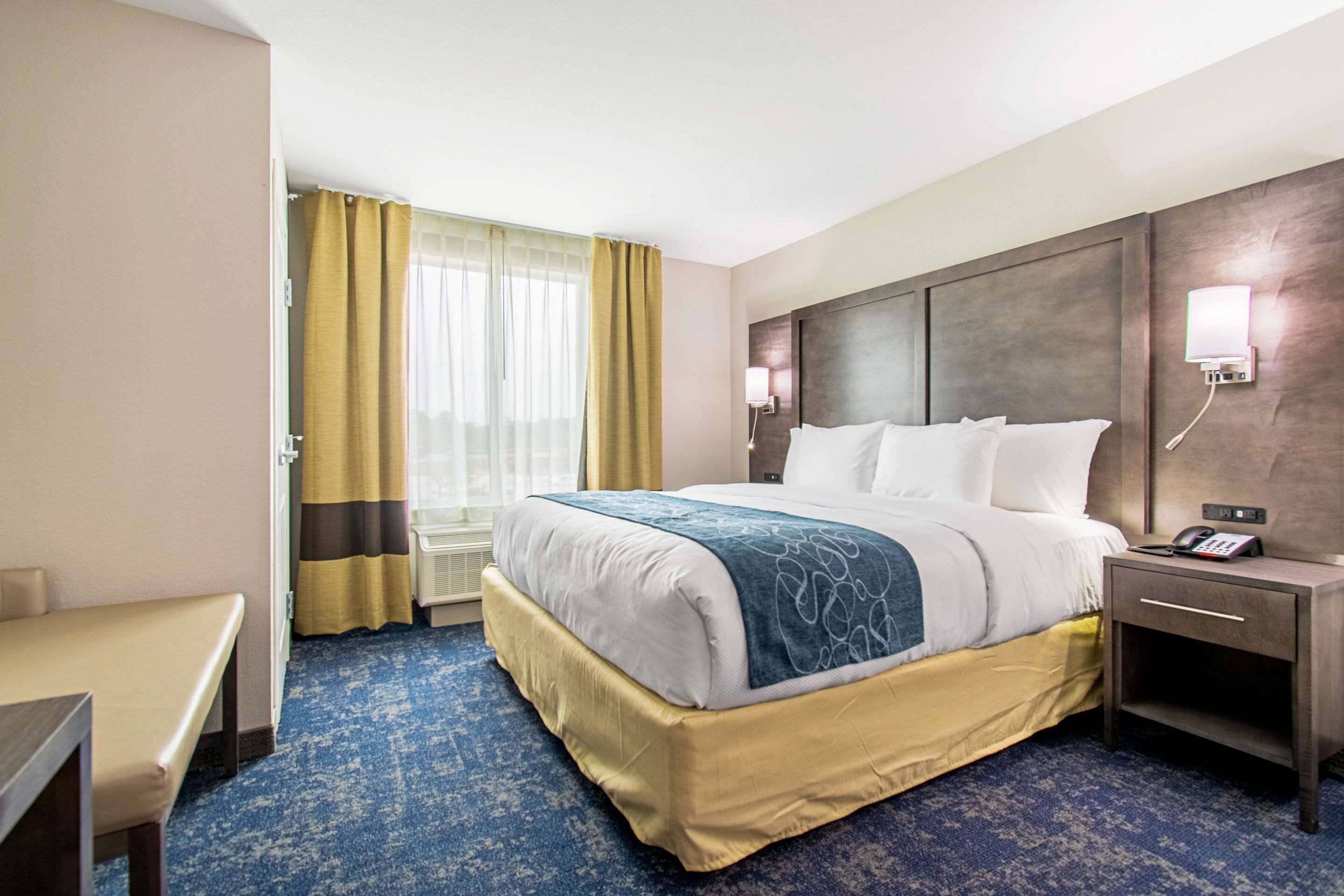 A hotel room with a large bed, bedside tables, a desk, and a window with curtains.