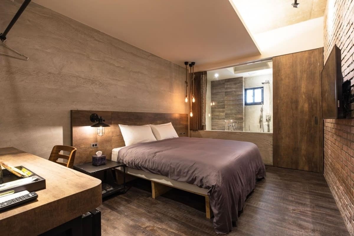 A modern bedroom with a large bed, a bedside table with a lamp, and a view of a bathroom through a glass door.