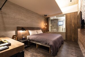 Une chambre à coucher moderne avec un grand lit, une table de chevet avec une lampe et une vue sur la salle de bain à travers une porte en verre.